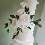 Classic tall three tier wedding cake decorated with flowers and foliage