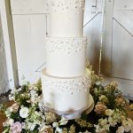 Stunning white three tier wedding cake with pearl decor surrounded by a floral wreath