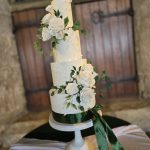 Three tier wedding cake in white and forest green decorated with icing flowers and foliage
