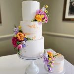 Bright three tier wedding cake with colourful floral decoration and a separate cutting cake in the same design
