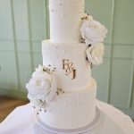 Peral and rose decorated white three tier wedding cake with bride and groom initials on the central layer