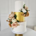Stunning three tier wedding cake with two white layers and a central gold layer with autumnal floral decoration