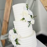 Butter iced three tier white wedding cake with white rose decoration