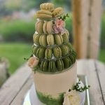 White wedding cake with pastel green decor and floral decoration topped with a stack of Macarons in shades of green