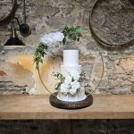 Three tier wedding cake with autumnal floral decoration and gold leaf detail surrounded by a floral hoop